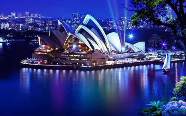 Night view of Sydney Opera House with city skyline and sailboat illuminations