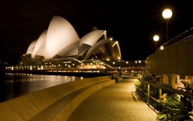 Night view of Sydney with the famous opera house illuminated and waterfront walkway visible