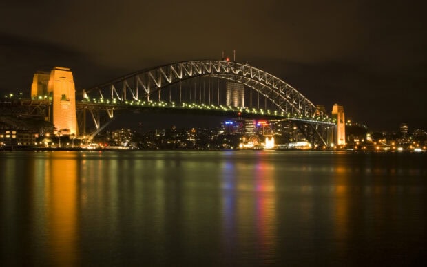 Sydney Harbour Bridge lit up at night with city lights reflecting on the water
