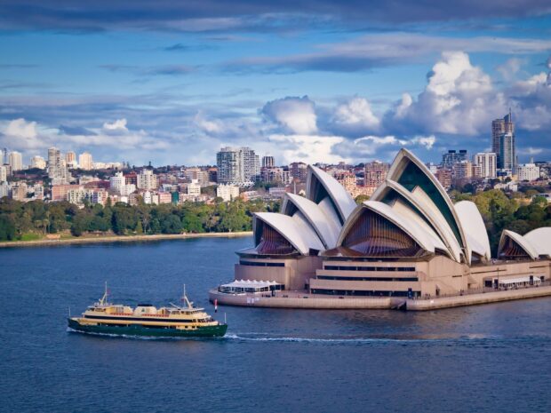A ferry passing by the iconic Sydney Opera House with the city skyline in the background