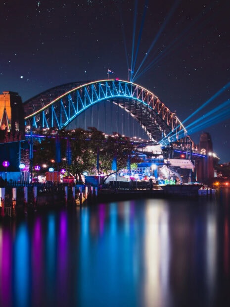 Sydney Harbour Bridge illuminated with colorful lights over calm water at night