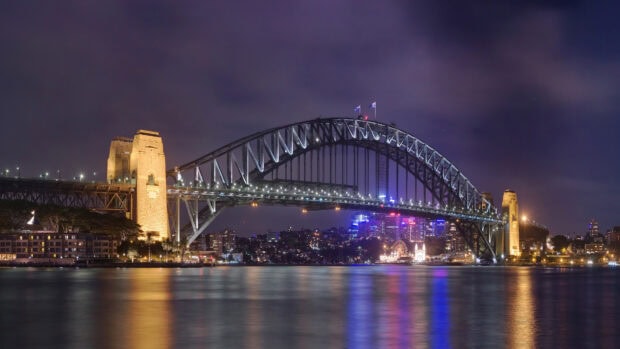 Sydney Harbour Bridge illuminated at night with city lights reflecting on water