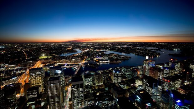 Sydney city skyline at dusk with vibrant lights and waterways visible