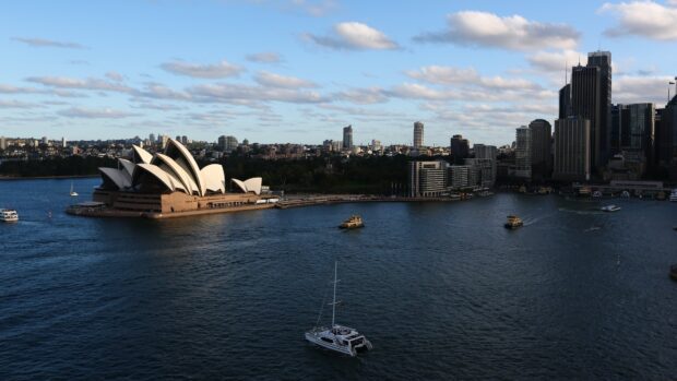 Sydney city skyline with iconic Opera House and boats on the harbor under a blue sky