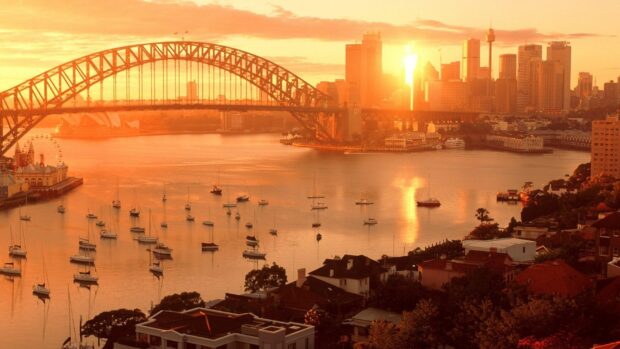 Sydney city skyline with harbor and bridge at sunset in warm golden light
