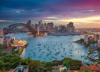 Sydney harbor with boats and a vibrant cityscape under a colorful sunset sky