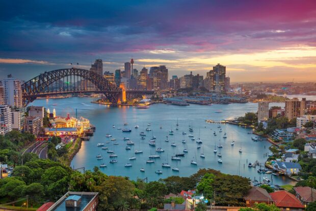 Sydney harbor with boats and a vibrant cityscape under a colorful sunset sky