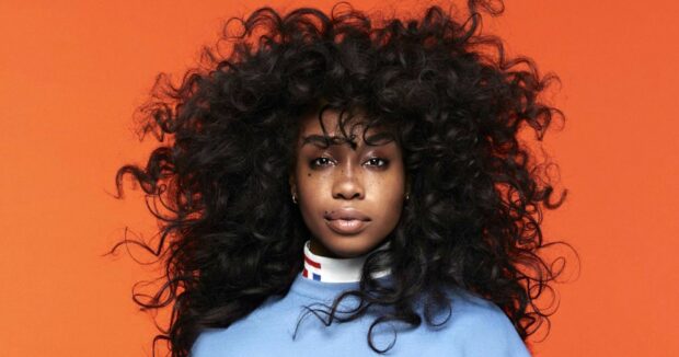 Sza with voluminous curly hair wearing a blue top against an orange background