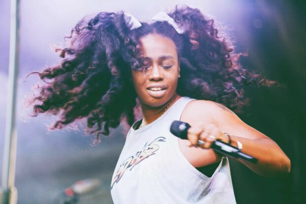Sza performing live on stage with flowing hair and holding a microphone