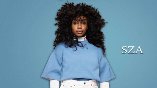 A close up portrait of Sza with natural curly hair and a blue top on a plain background