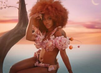 A woman with natural curly hair wearing floral outfit posing by the tree at sunset