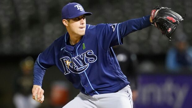 A Tampa Bay Rays player pitching in a dark blue uniform during a nighttime game