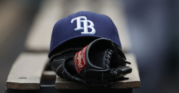 A baseball glove and Tampa Bay Rays cap resting on a wooden bench