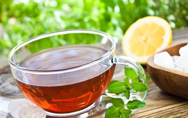 A glass cup of tea with fresh mint leaves and lemon slice on a wooden table