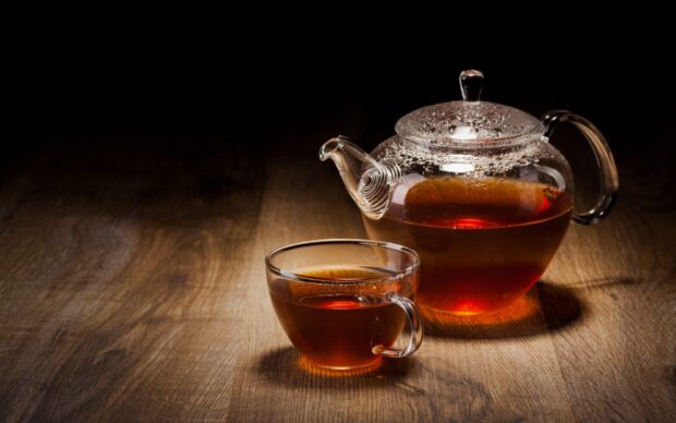A glass teapot and cup filled with hot brewed tea on a wooden surface