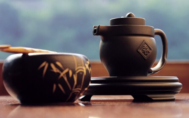 A traditional tea pot with intricate design sitting on a wooden stand near a decorated tea cup