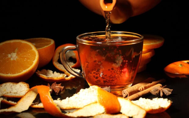 Fresh tea being poured into a glass cup surrounded by orange slices cinnamon sticks and star anise