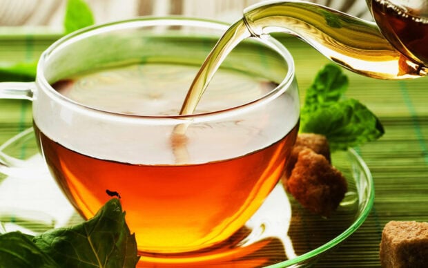 Tea being poured into a clear cup surrounded by fresh mint leaves and sugar cubes