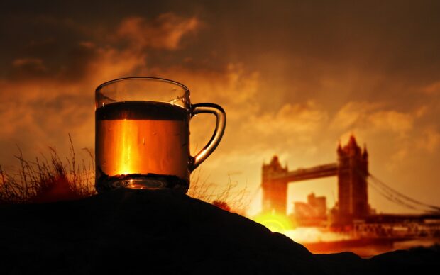 A clear cup of tea glowing orange with a city bridge silhouette in the background at sunset