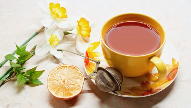 A close up of a citrus tea with tea infuser and flowers on a marble surface