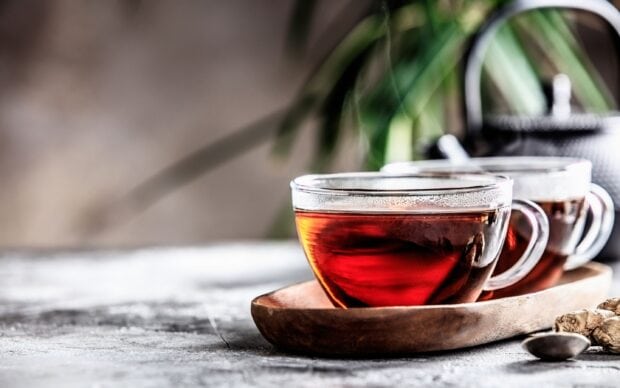 A close up of tea in clear glass cups on a wooden tray with a teapot in the background