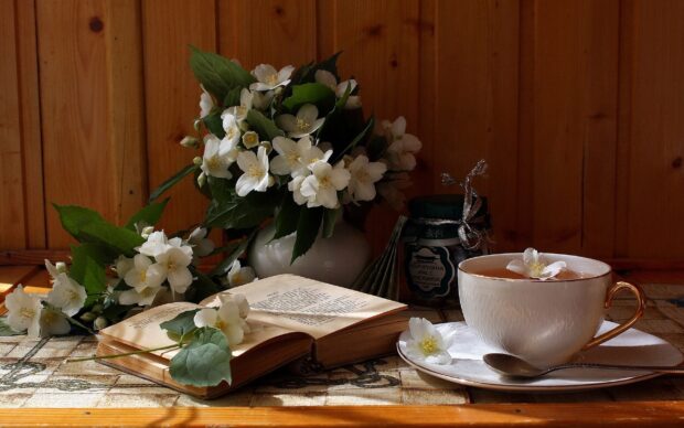 A bouquet of jasmine flowers next to an open book and a cup of tea on a wooden table