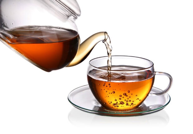 A clear teapot pouring fresh tea into a transparent glass teacup with saucer