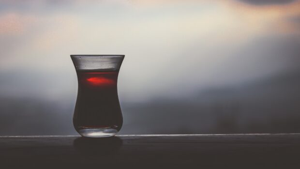 A clear glass filled with tea placed on a wooden surface against a blurred background