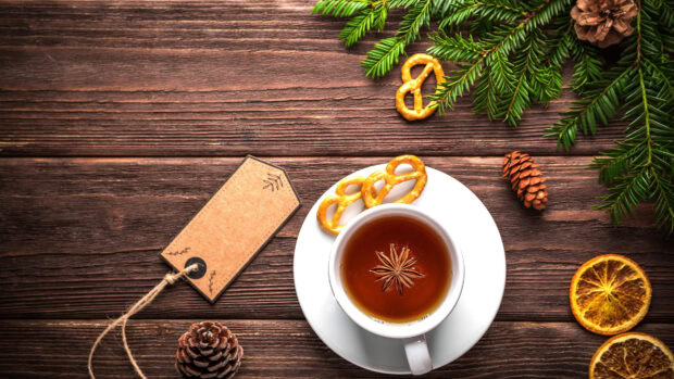 A cup of tea with star anise on a wooden table with pine cones and dried oranges