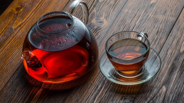 A glass teapot and a cup of tea on a wooden table with steam rising