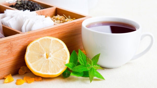 Fresh tea with lemon slice and mint leaves next to a wooden box of tea bags