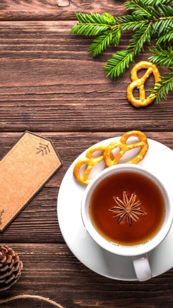 A star anise floating in tea with pretzels on a wooden table surrounded by pine leaves