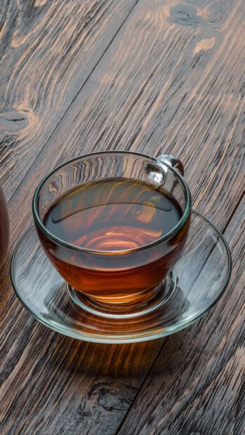 A clear glass cup filled with tea placed on a wooden surface