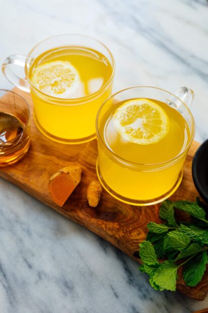 Two cups of lemon turmeric tea on a wooden board with fresh mint leaves