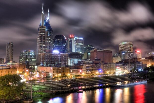 Nighttime cityscape of Tennessee skyline with illuminated buildings and river reflections