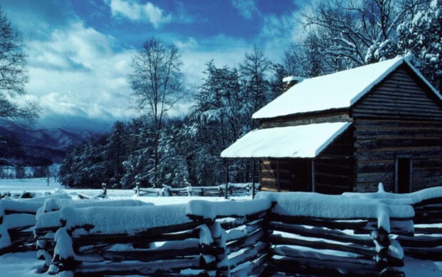 Snow covered cabin and fence in Tennessee winter landscape with mountains and trees