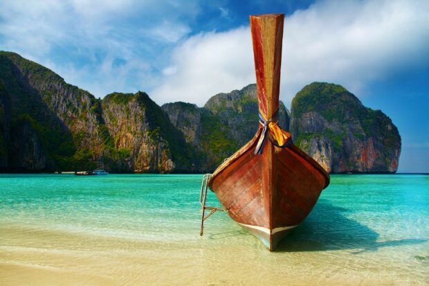 A traditional longtail boat near the shore in Thailand with turquoise water and limestone cliffs in the background