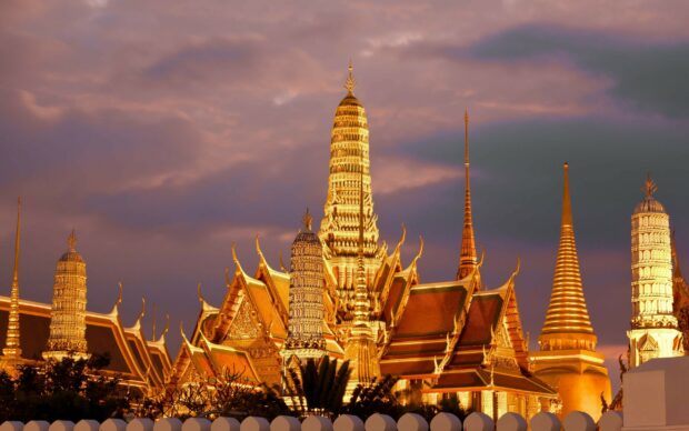 The grand golden temple architecture in Thailand at dusk with a dramatic sky