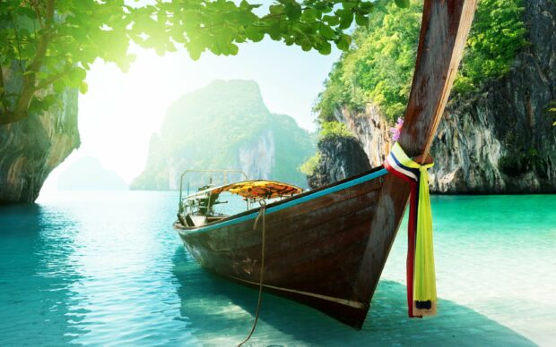 Traditional long tail boat with colorful ribbons floating on clear turquoise water in Thailand bay surrounded by limestone cliffs and green foliage