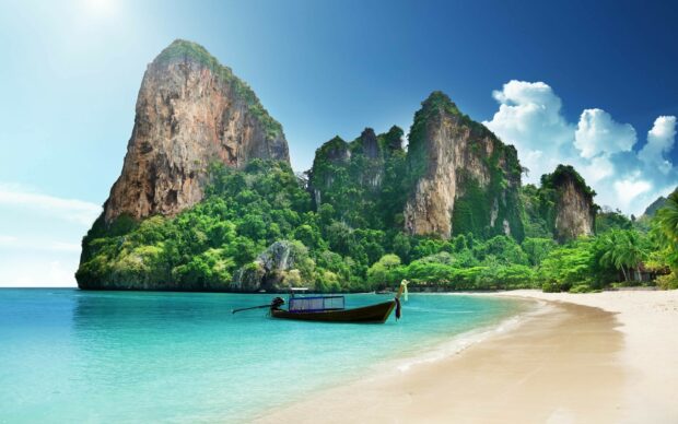 Traditional longtail boat near lush cliffs in Thailand sea landscape