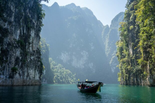 Traditional longtail boat sailing through limestone cliffs in Thailand scenery