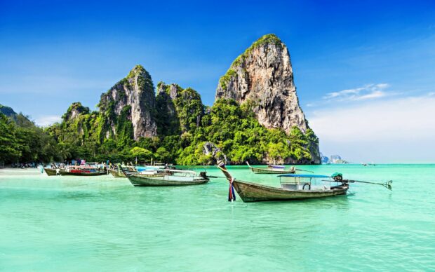 Traditional longtail boats floating on turquoise water near limestone cliffs in Thailand