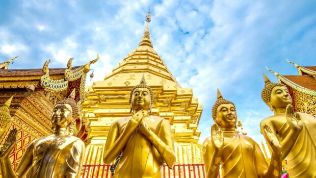 Golden Buddha statues with temple architecture in Thailand under blue sky