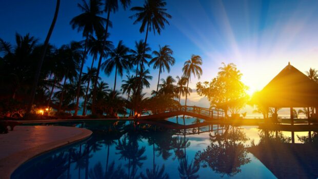 Tropical resort scene in Thailand with palm trees and a glowing sunset over the pool reflection