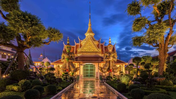 Traditional Thai temple guarded by giant statues with vibrant evening sky