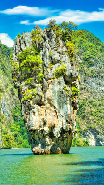 Unique Thailand rock formation surrounded by lush greenery and calm water in summer