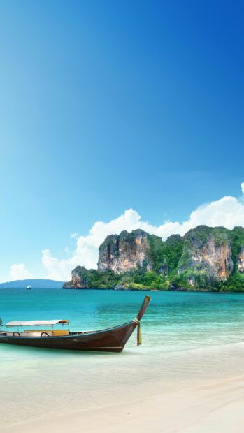 Traditional Thailand boat near a sandy beach with limestone cliffs in the background