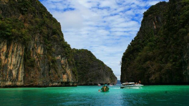 Turquoise water between limestone cliffs in Thailand with tourists on boats