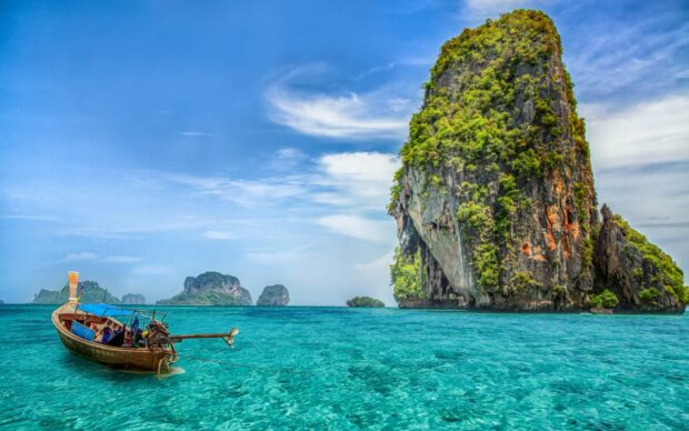 A traditional longtail boat floats near limestone cliffs in Thailand coast