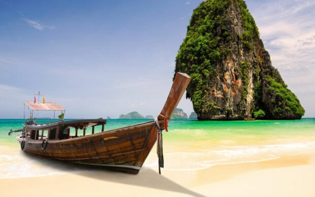 A traditional longtail boat near a limestone cliff on a beautiful Thailand beach